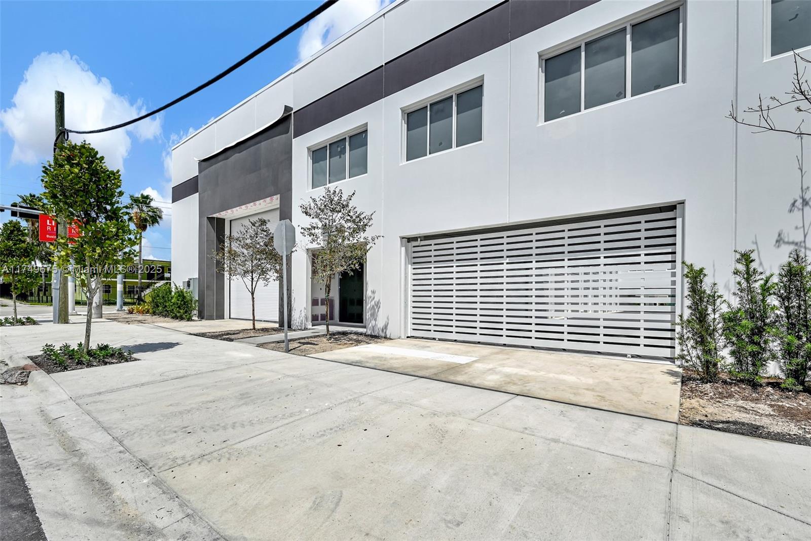 A modern commercial building exterior features white walls, dark accents, and slatted metal garage doors — 210 NE 68th St # 1, Miami FL 33138, MIAMI, FL