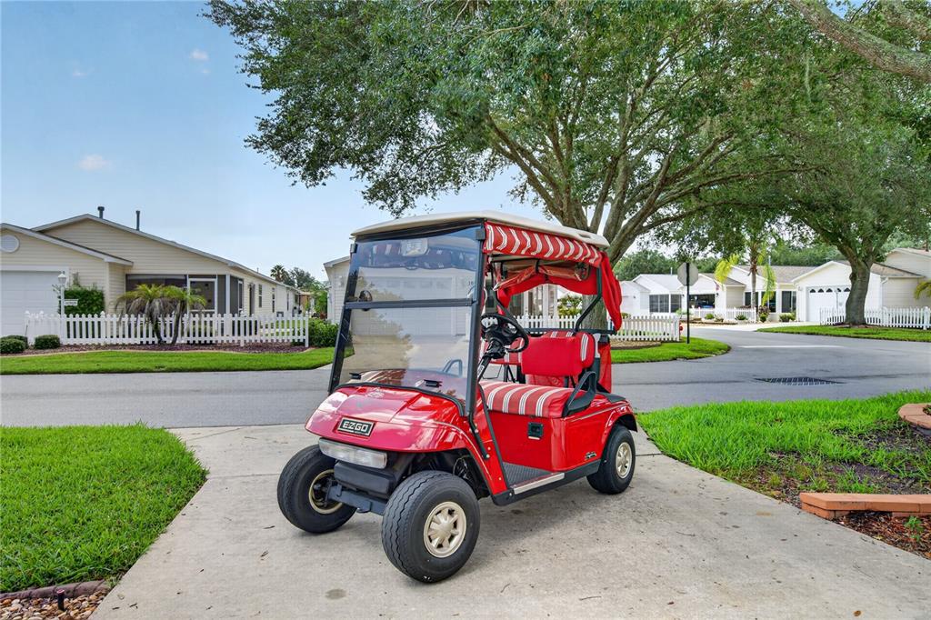 A red EZ-GO golf cart sits on a concrete driveway in front of suburban houses — 16970 SE 94TH SUNNYBROOK CIRCLE, THE VILLAGES, FL