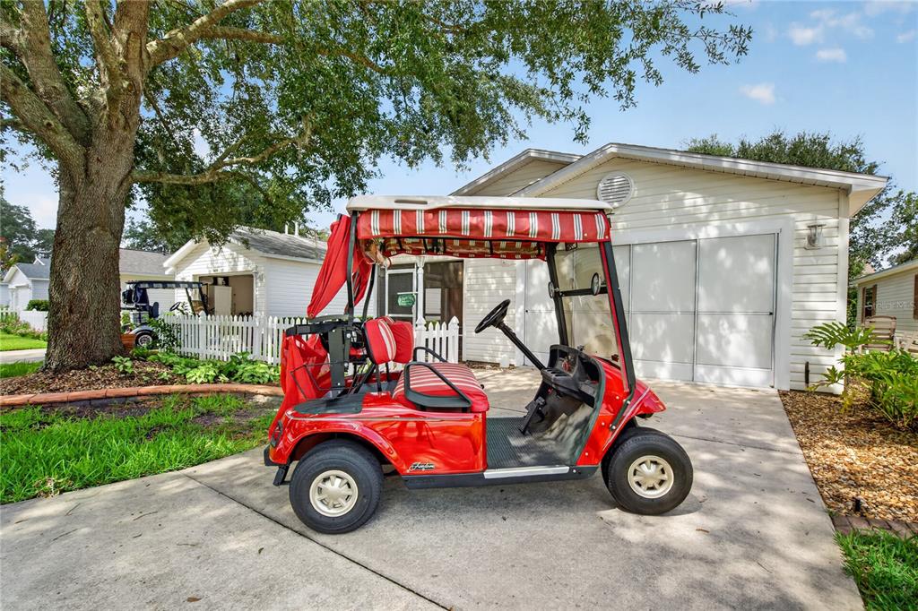 A red golf cart with a striped canopy sits on a concrete driveway before a house — 16970 SE 94TH SUNNYBROOK CIRCLE, THE VILLAGES, FL