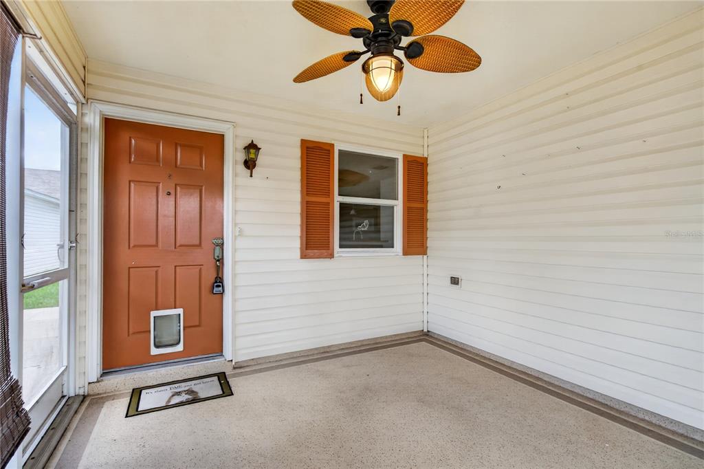 A covered porch features a brown door with a pet door, siding, and a ceiling fan — 16970 SE 94TH SUNNYBROOK CIRCLE, THE VILLAGES, FL