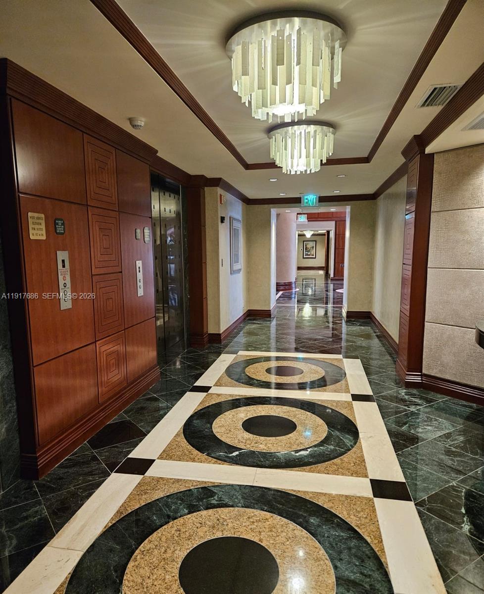 A hallway with patterned marble floors, wood-paneled walls, and two tiered glass chandeliers — 21050 Point Pl # 501, Aventura FL 33180, AVENTURA, FL
