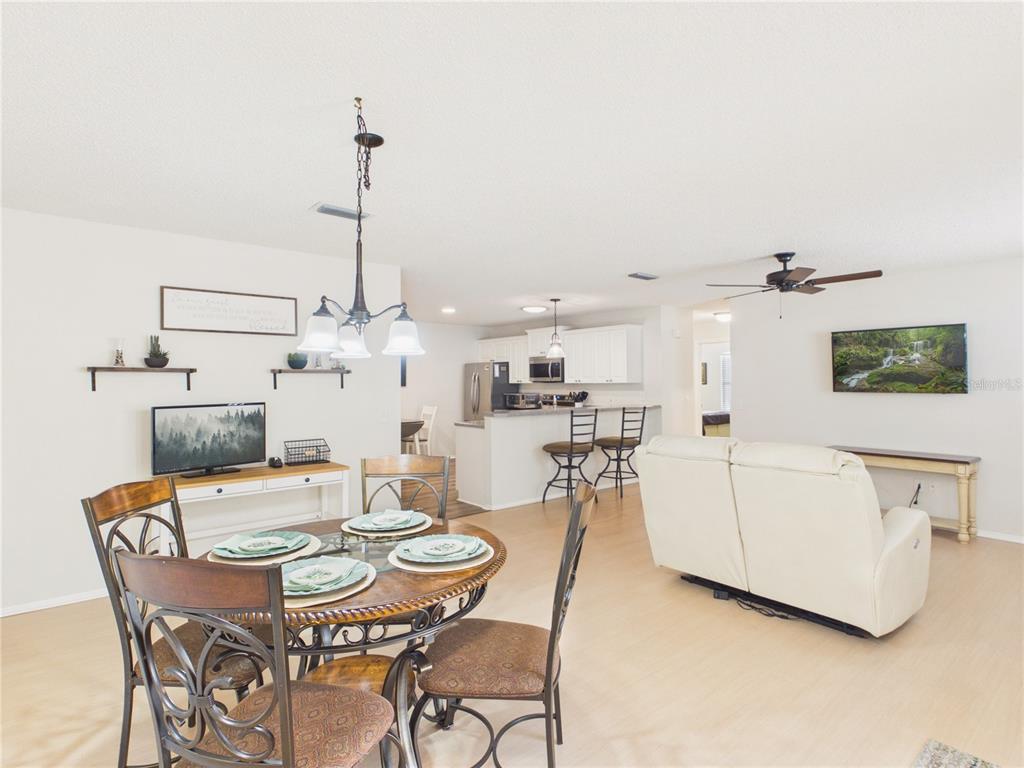 An open-concept living and dining area features light wood-look flooring, a kitchen island, and furniture — 746 ANGELITA AVE, THE VILLAGES, FL