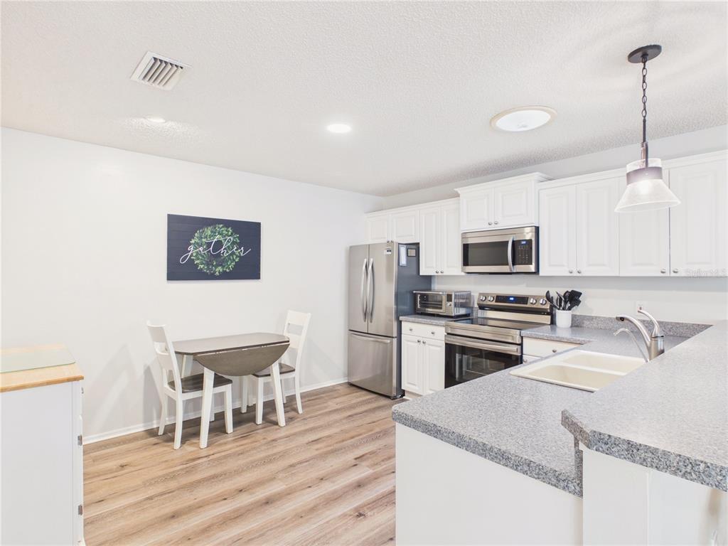 A kitchen features white cabinets, stainless steel appliances, a gray countertop, and a small dining area — 746 ANGELITA AVE, THE VILLAGES, FL