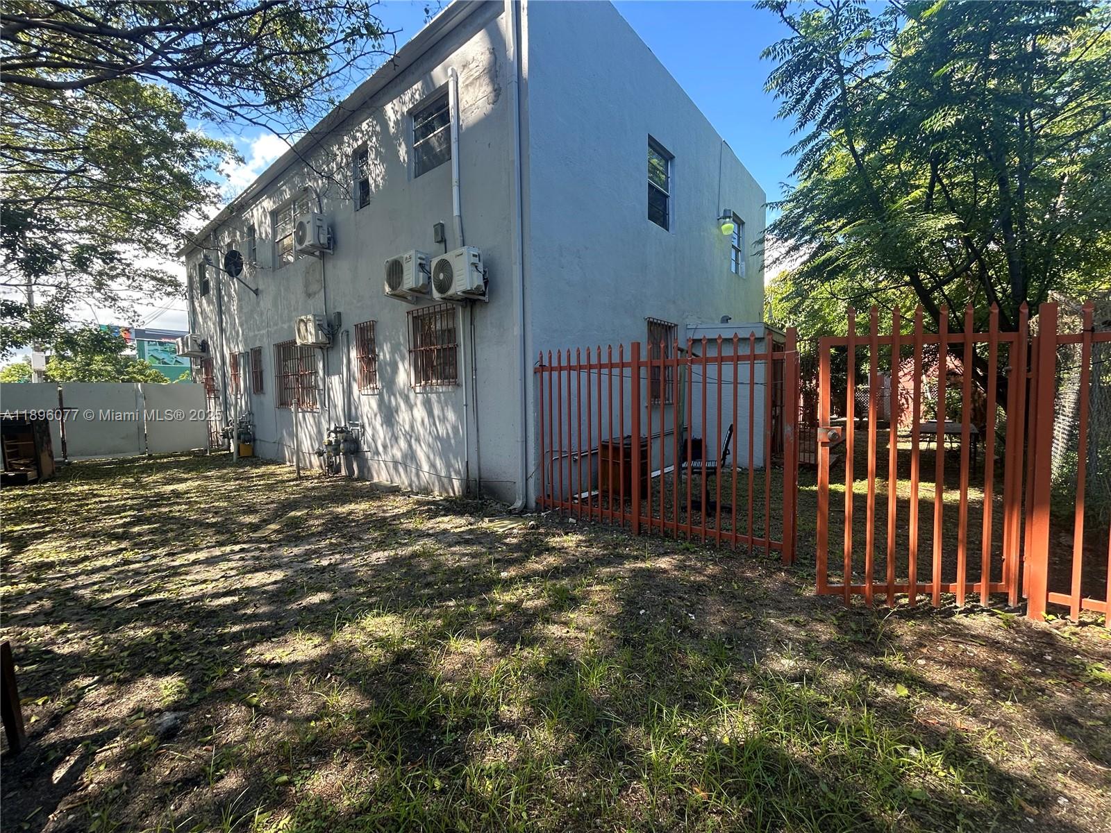A two-story gray building with multiple wall-mounted air conditioning units stands behind a red fence — 2015 NW 6th Pl, Miami FL 33127, MIAMI, FL