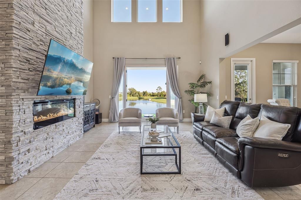 A living room features a stone fireplace, a large television, and a view of water — 9207 BUSACO PARK WAY, WINTER GARDEN, FL