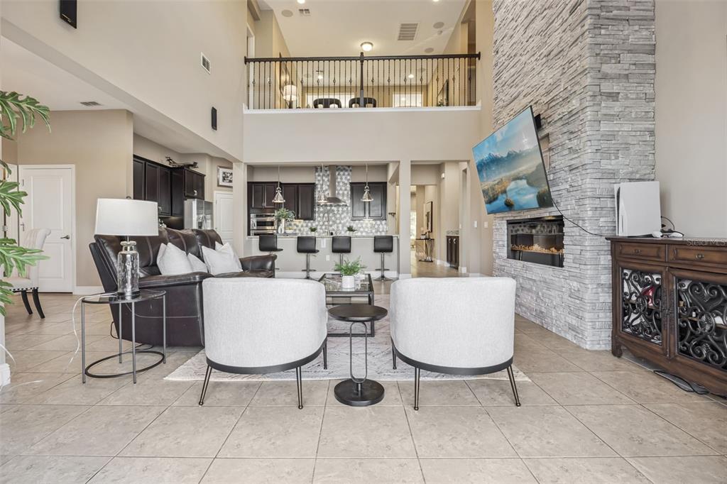 A living room with a stone fireplace, high ceilings, and an open kitchen with bar seating — 9207 BUSACO PARK WAY, WINTER GARDEN, FL