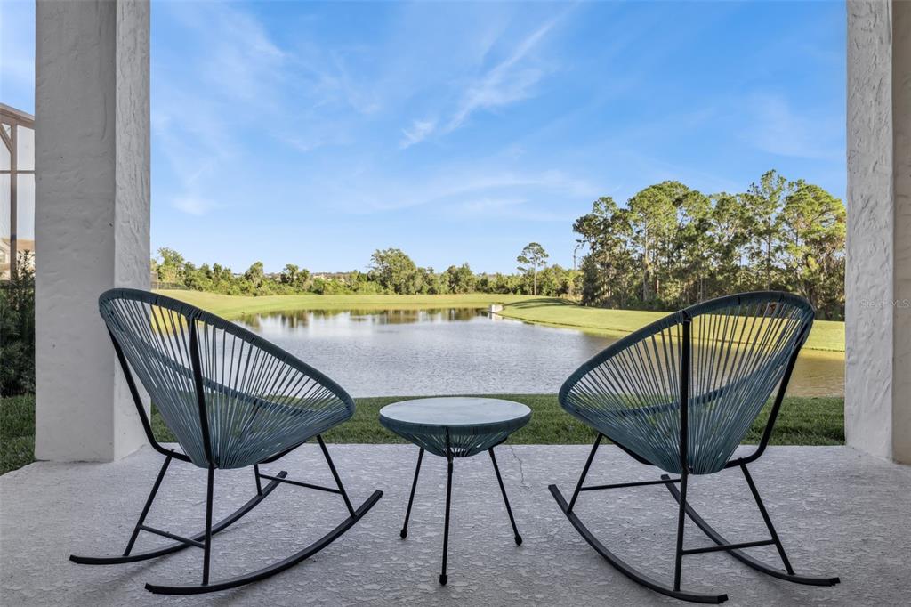 Two blue rocking chairs and a small table sit on a covered patio overlooking a lake — 9207 BUSACO PARK WAY, WINTER GARDEN, FL