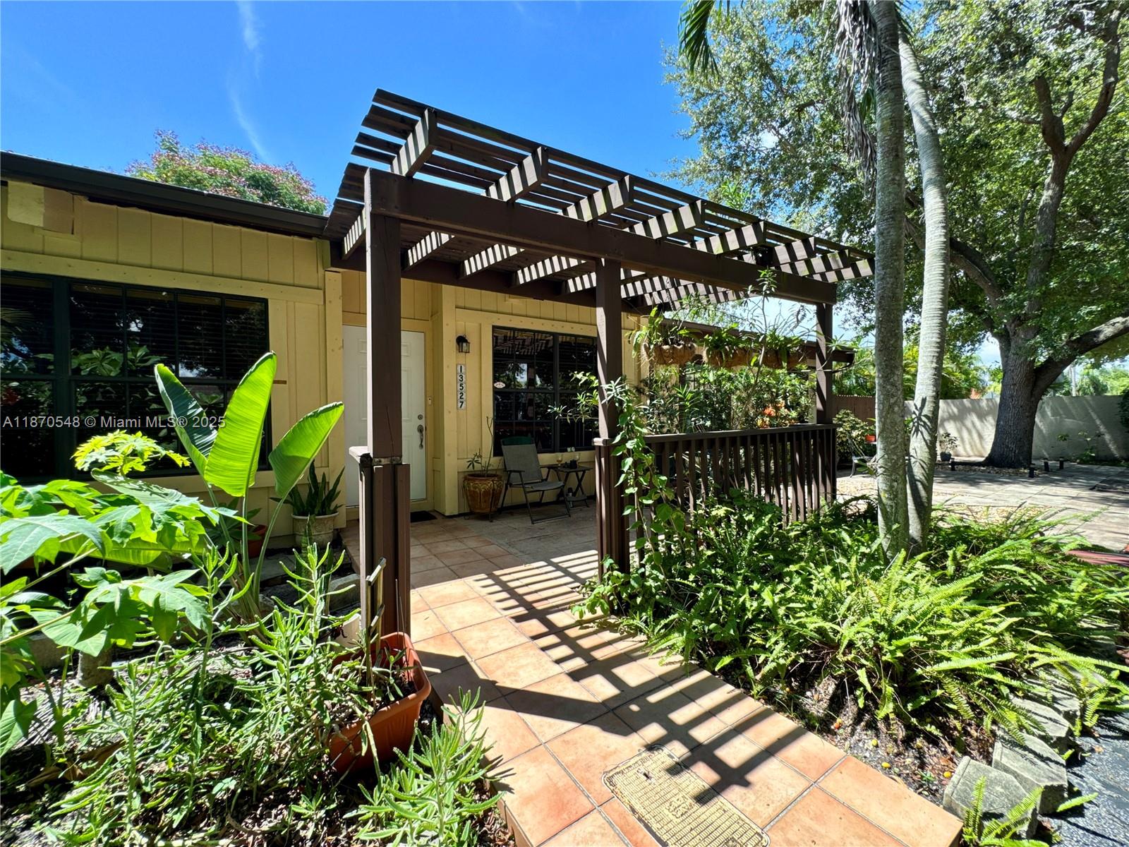 A wooden pergola covers the tiled entryway and porch of a yellow house — 13527 SW 101st Ln, Miami FL 33186, MIAMI, FL
