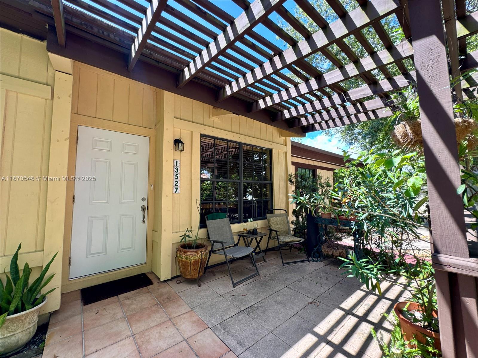 A yellow house exterior features a white front door, a pergola, and a tiled patio — 13527 SW 101st Ln, Miami FL 33186, MIAMI, FL