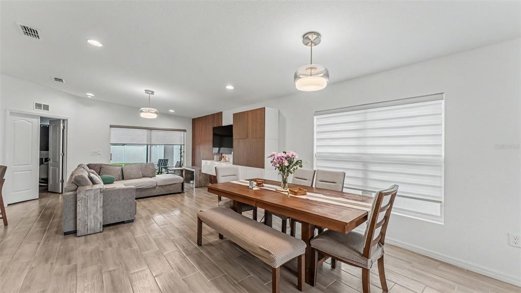An open-concept living and dining area features wood-look tile flooring and modern light fixtures — 1201 PINTAIL PLACE, LAKELAND, FL
