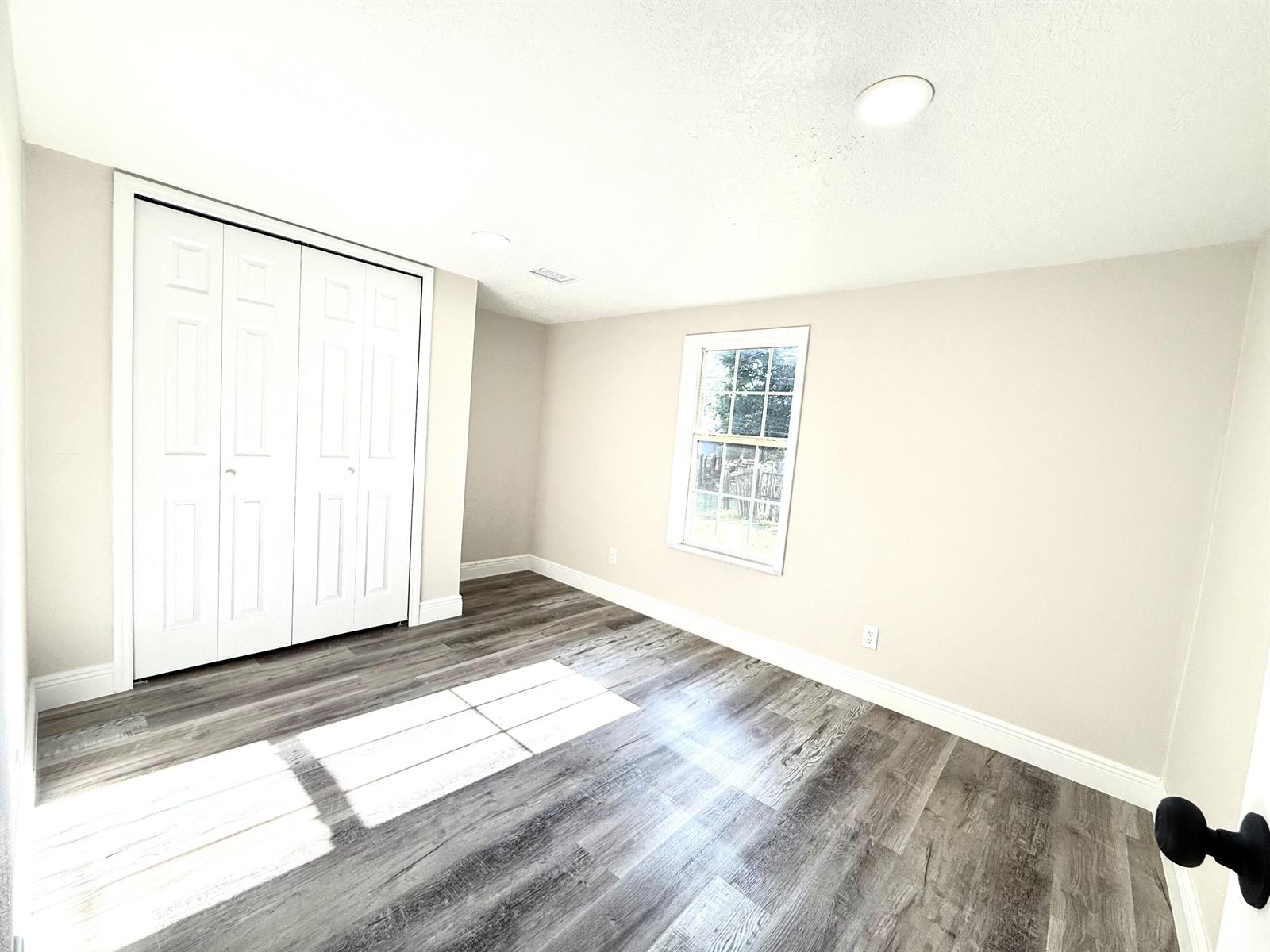 An empty bedroom features light-colored walls, wood-look flooring, a white closet, and a single window — 1465 NW 43rd Avenue, Okeechobee FL 34972, OKEECHOBEE, FL