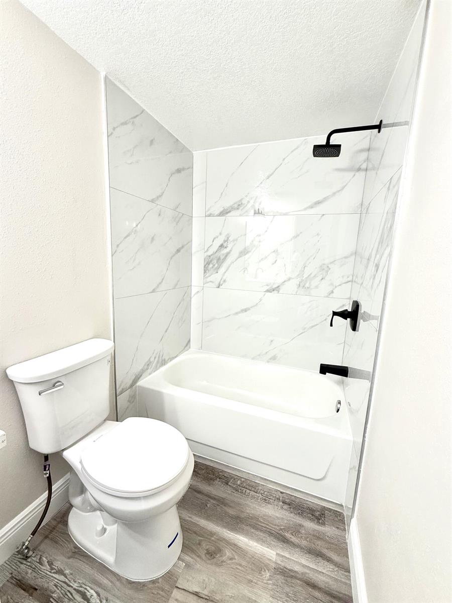 A bathroom features a white toilet, a white bathtub, and white marble-patterned wall tiles — 1465 NW 43rd Avenue, Okeechobee FL 34972, OKEECHOBEE, FL