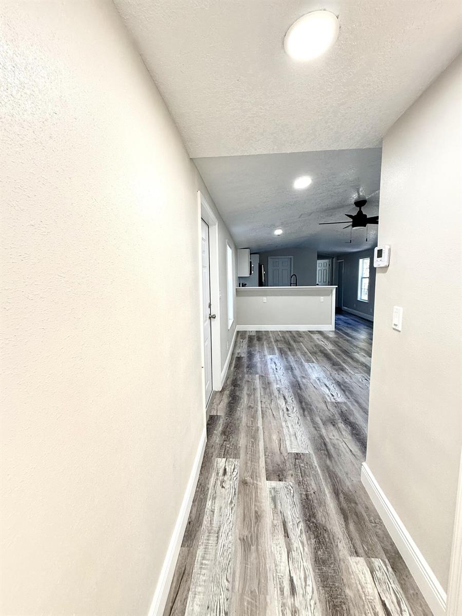 A hallway with wood-look flooring leads to an open-concept kitchen and living area — 1465 NW 43rd Avenue, Okeechobee FL 34972, OKEECHOBEE, FL