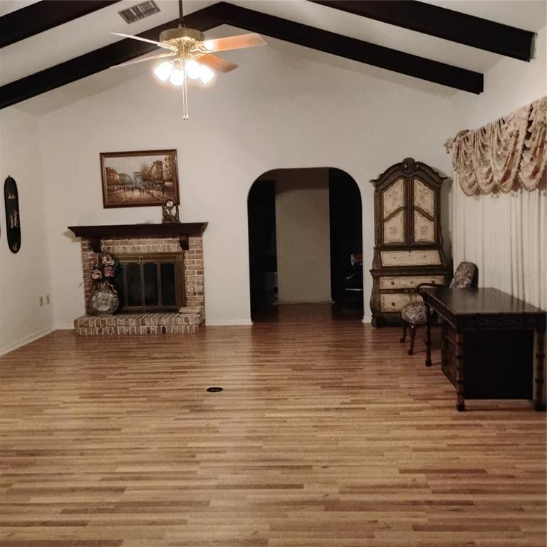 A living room features a brick fireplace, vaulted ceiling with exposed beams, and wood flooring — 8943 SILVER LAKE DRIVE, LEESBURG, FL