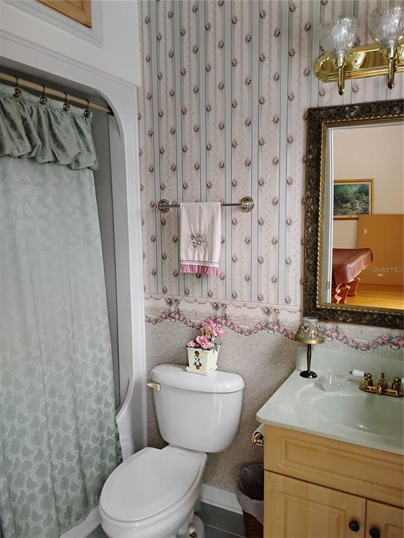 A bathroom features floral wallpaper, a vanity with a sink, a toilet, and a shower curtain — 8943 SILVER LAKE DRIVE, LEESBURG, FL