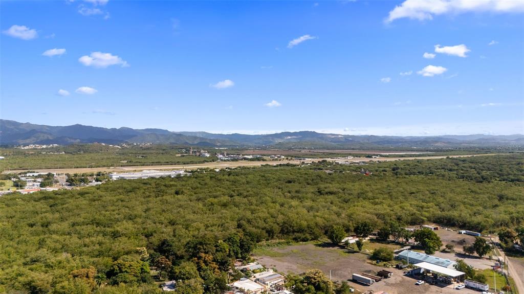 An aerial view shows a large, forested area with a distant runway and mountain range — SECTOR VALLAS TORRES LOT 2, PONCE, PR