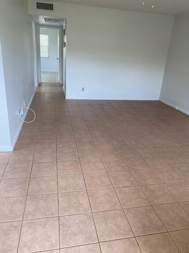 An empty room with light-colored walls and tan square floor tiles leads to a hallway — 99 Mansfield C # 99, Boca Raton FL 33434, BOCA RATON, FL