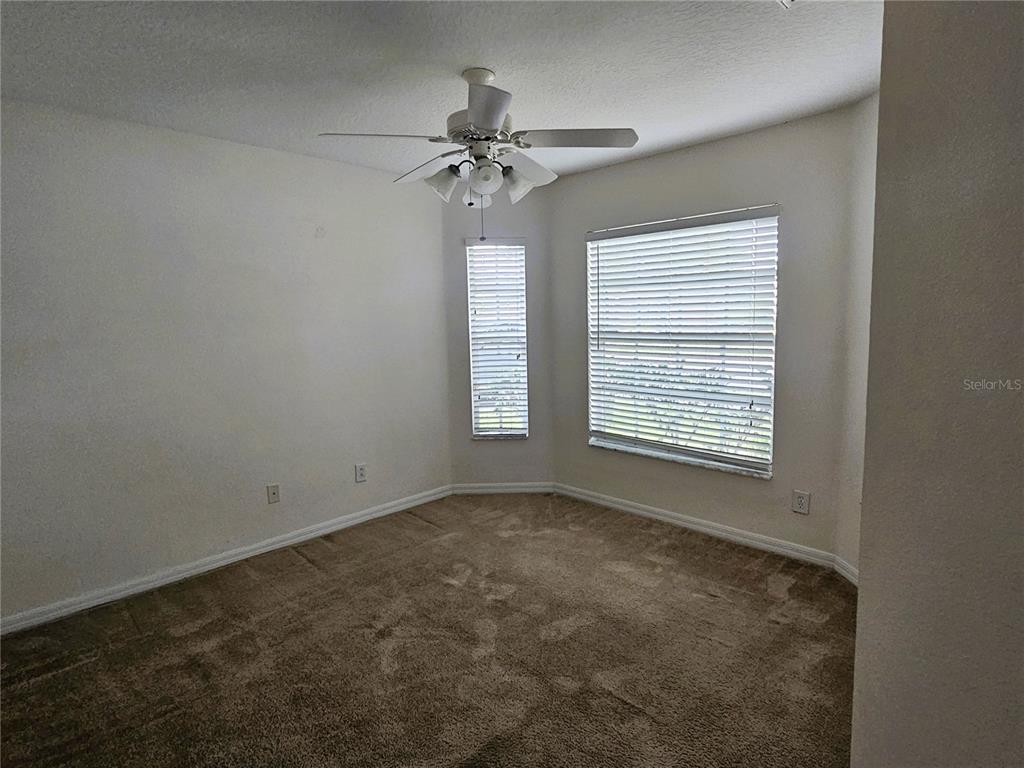 An empty bedroom features beige carpeting, white walls, a ceiling fan, and two windows — 3220 CLOVER BLOSSOM CIRCLE, LAND O LAKES, FL