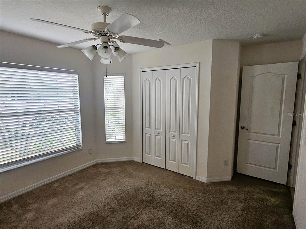 A bedroom with beige carpet, white walls, a ceiling fan, a closet, and two windows — 3220 CLOVER BLOSSOM CIRCLE, LAND O LAKES, FL