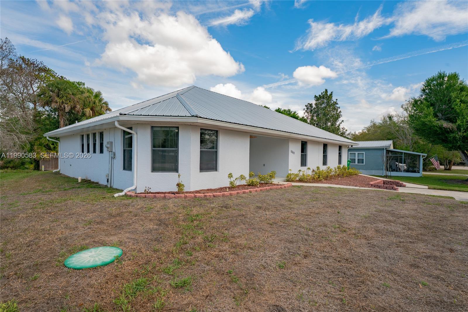 A white, single-story house with a metal roof and a recessed entryway sits on grass — 1063 Mayford Lake Rd, Moore Haven FL 33471, MOORE HAVEN, FL