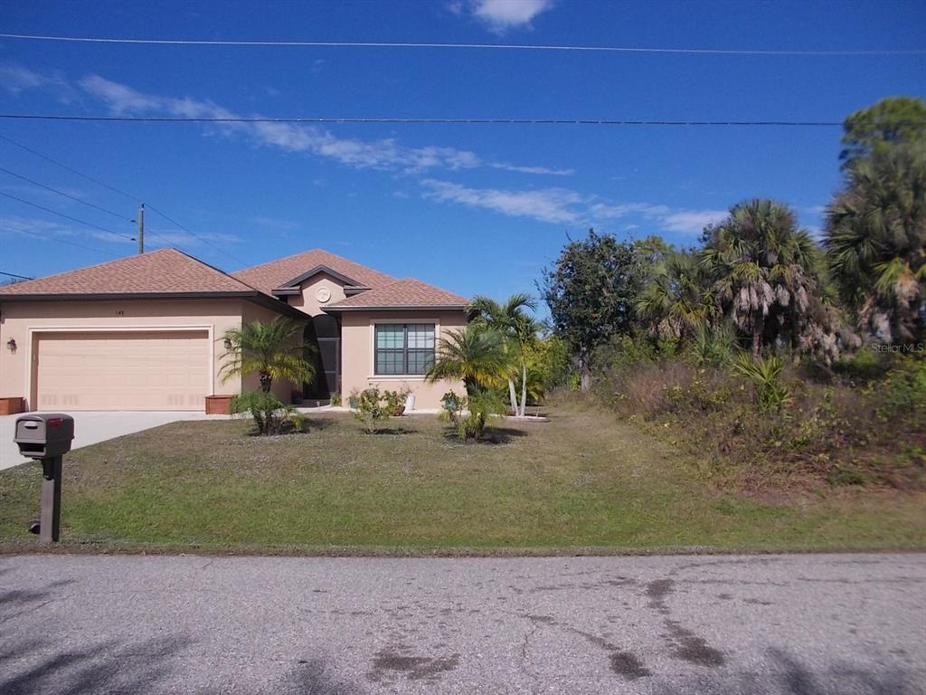 A single-story house with a tan exterior, a two-car garage, and an adjacent vacant lot — 147 YELLOW PINE DRIVE, ROTONDA WEST, FL