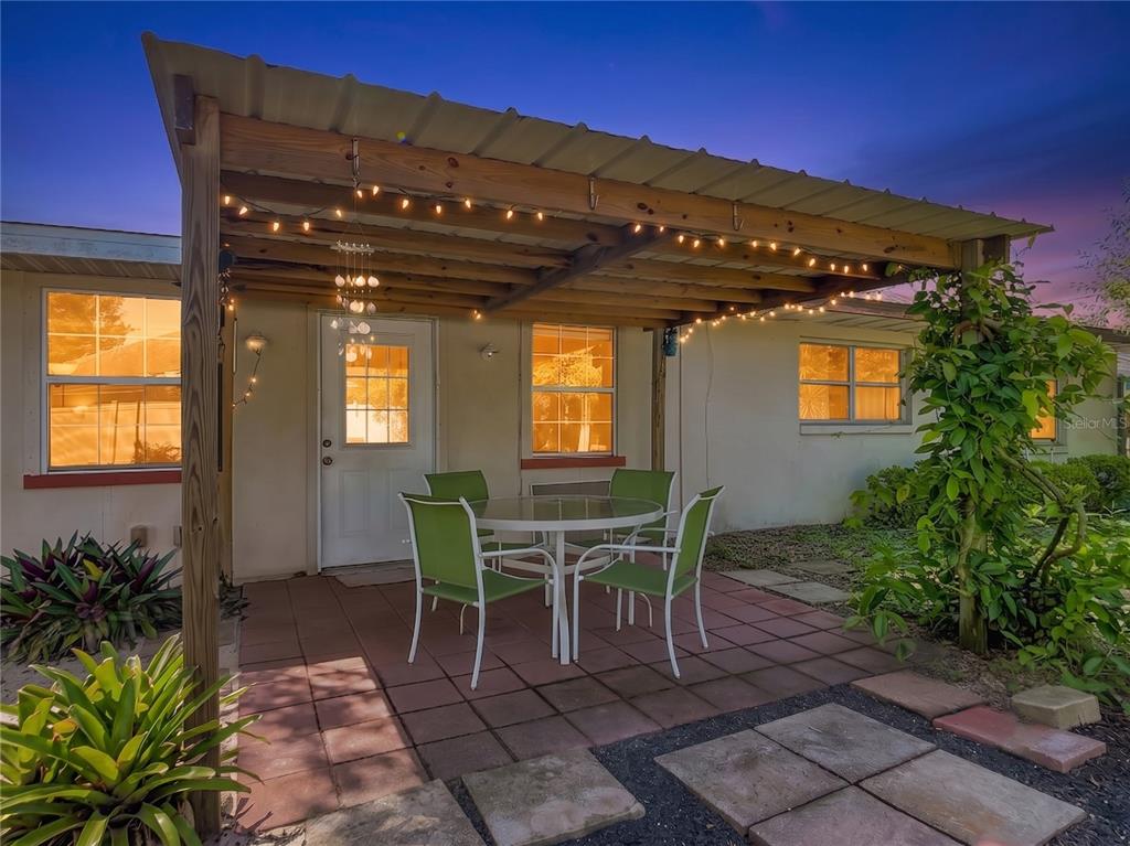 A patio with a wooden pergola, string lights, and a dining set sits outside a house — 1468 CORONET DRIVE, DELTONA, FL