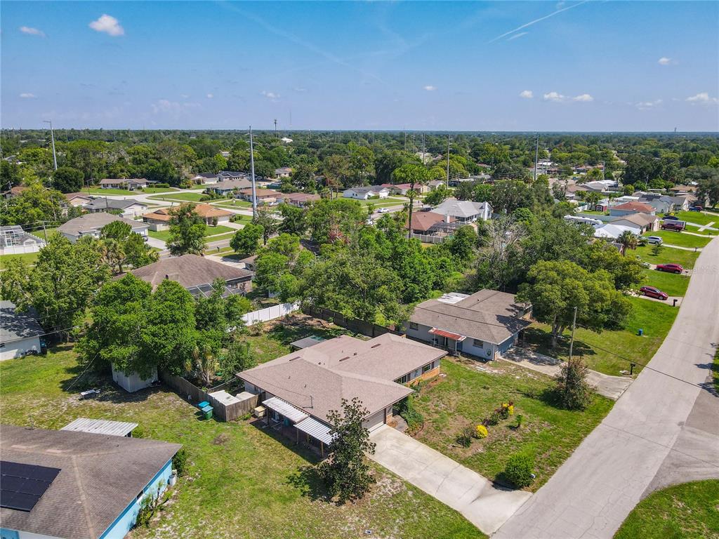 An aerial view shows a suburban neighborhood with single-story houses, green lawns, and trees — 1468 CORONET DRIVE, DELTONA, FL