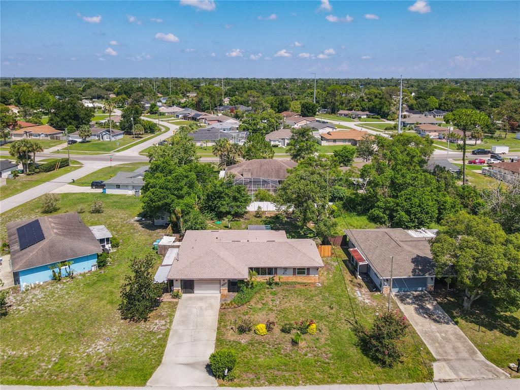 An aerial view shows a suburban neighborhood with single-story houses, driveways, and surrounding trees — 1468 CORONET DRIVE, DELTONA, FL