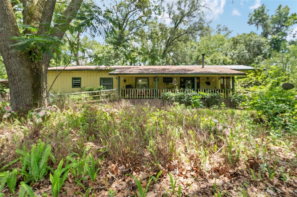 A yellow single-story house with a covered front porch sits behind overgrown vegetation and trees — 20104 NW 184TH TERRACE, HIGH SPRINGS, FL