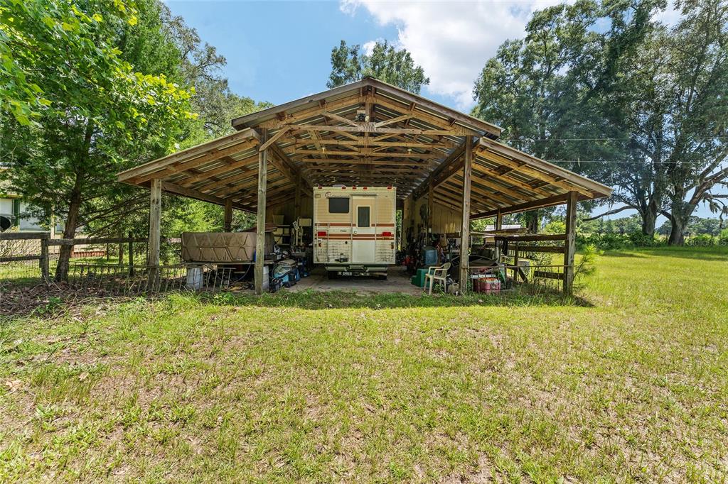 A metal-roofed carport shelters a recreational vehicle on a grassy lot with surrounding trees — 20104 NW 184TH TERRACE, HIGH SPRINGS, FL