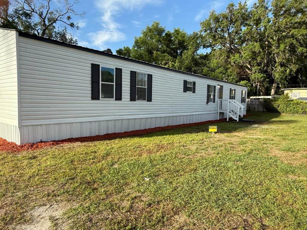 A white mobile home with black shutters sits on a grassy lot with red mulch — 3464 SE 91ST PLACE, OCALA, FL