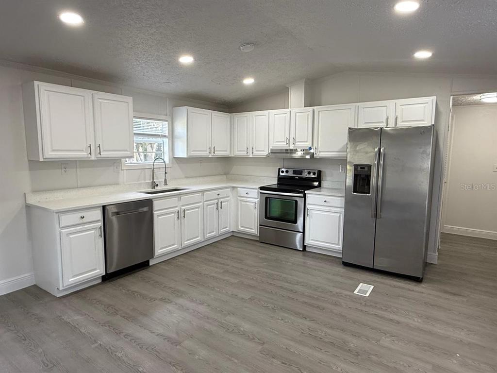 A kitchen features white cabinets, stainless steel appliances, and light gray wood-look flooring — 3464 SE 91ST PLACE, OCALA, FL