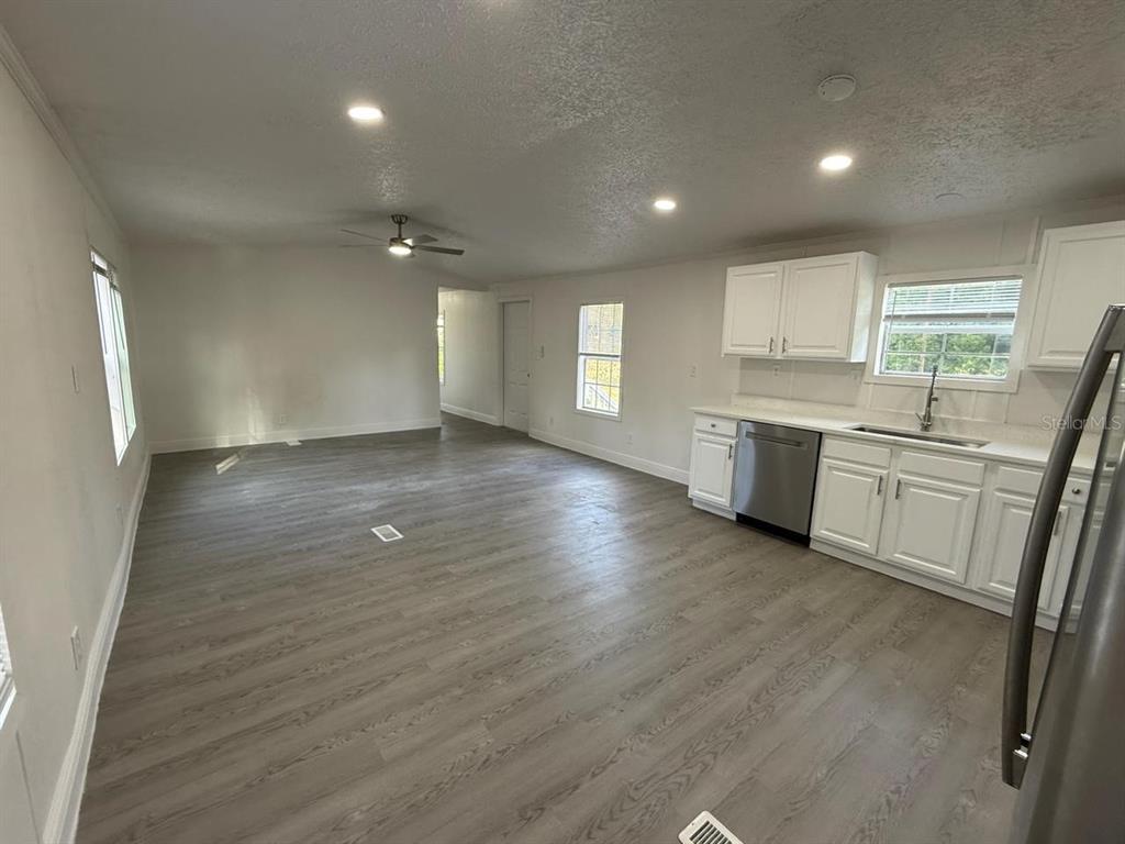 An open-concept kitchen and living area with white cabinets, stainless appliances, and wood-look flooring — 3464 SE 91ST PLACE, OCALA, FL