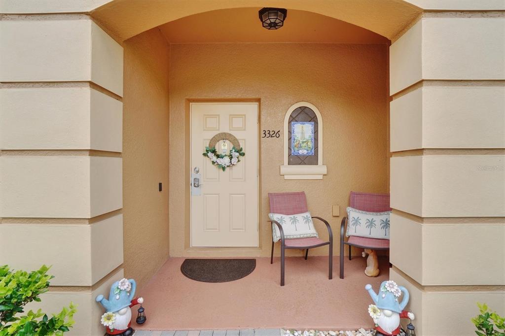 A covered entryway features a beige door, two chairs, and decorative gnome statues — 3326 CALABRIA AVENUE, DAVENPORT, FL