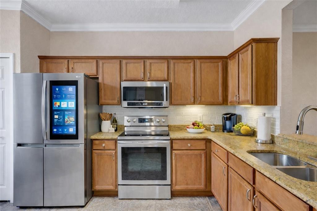 A kitchen features wood cabinets, granite countertops, stainless steel appliances, and a smart refrigerator — 3326 CALABRIA AVENUE, DAVENPORT, FL