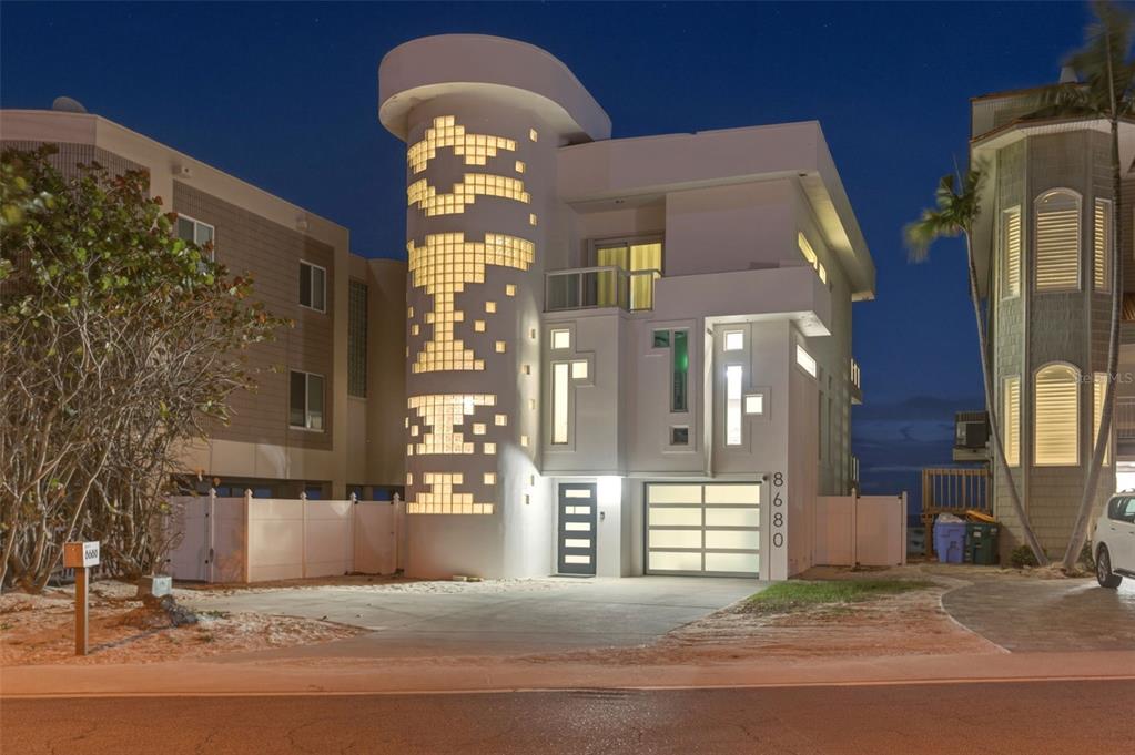 A modern house with a cylindrical glass block tower stands at twilight — 8680 W GULF BOULEVARD, TREASURE ISLAND, FL