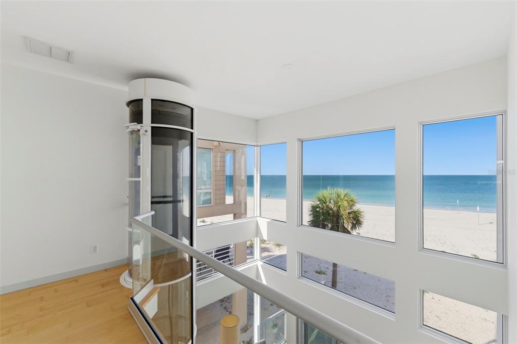 A modern interior with a glass elevator overlooking a beach and the ocean — 8680 W GULF BOULEVARD, TREASURE ISLAND, FL
