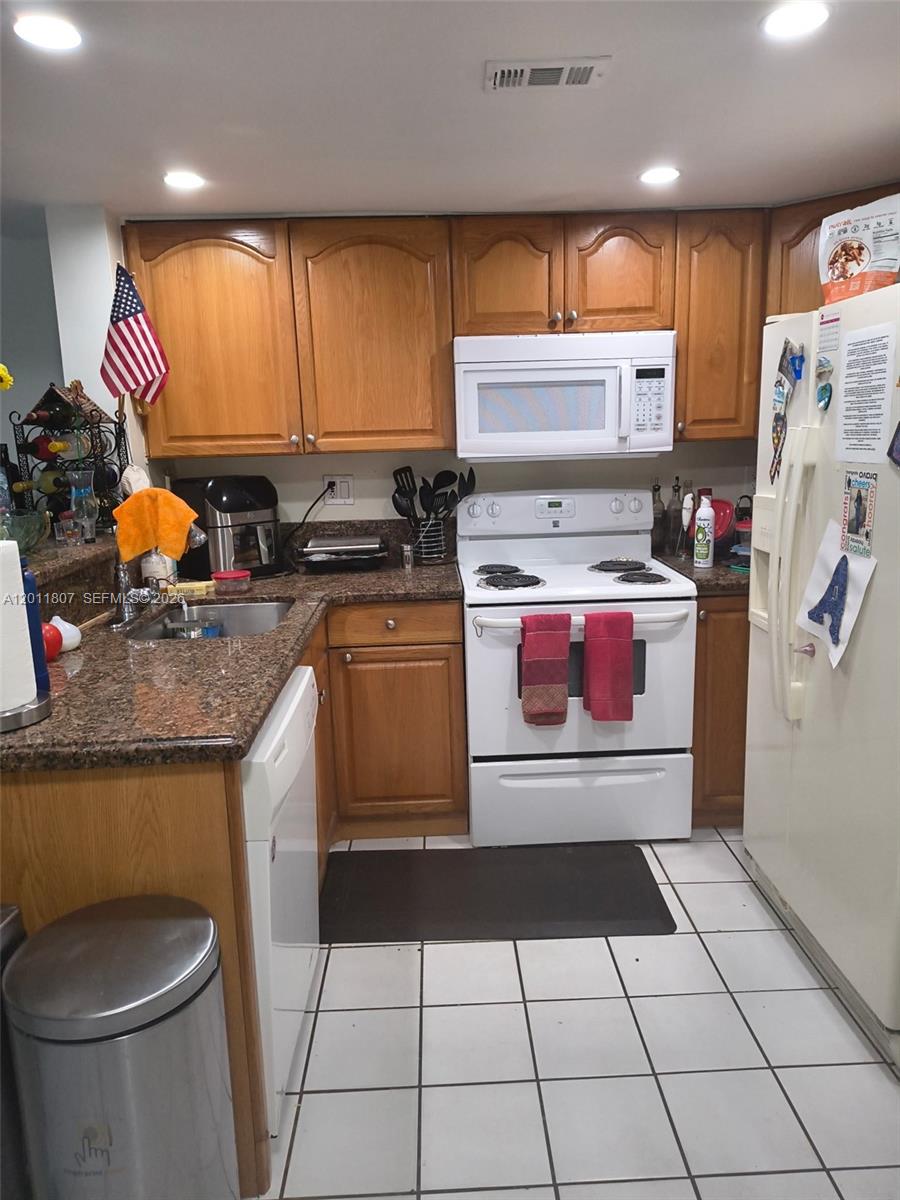 A kitchen features wood cabinets, granite countertops, white appliances, and white tiled flooring — 650 NW 86th Pl # 101, Miami FL 33126, MIAMI, FL