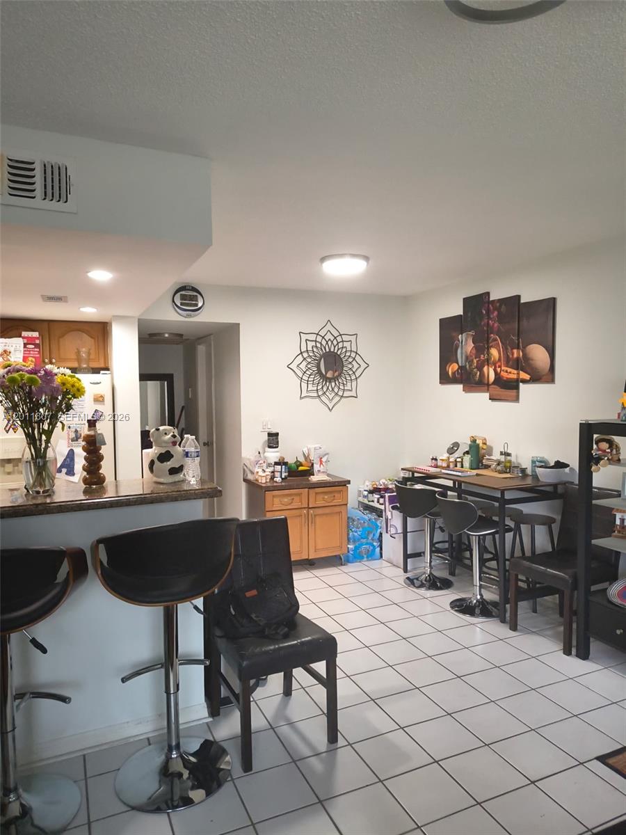 A kitchen and dining area with tile floors, a breakfast bar, and wall art — 650 NW 86th Pl # 101, Miami FL 33126, MIAMI, FL