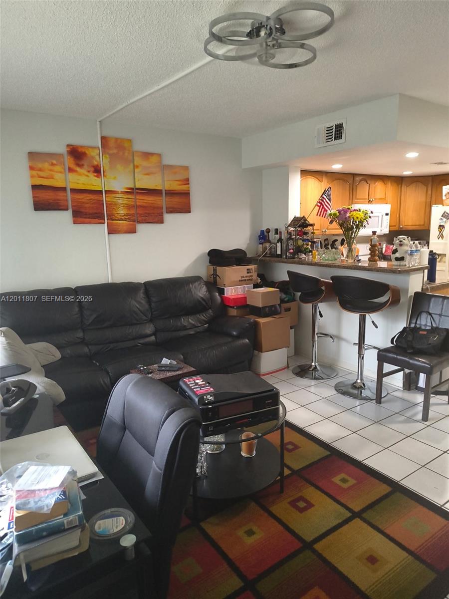 A living room features a black leather sofa, a multi-panel sunset wall art, and a kitchen bar — 650 NW 86th Pl # 101, Miami FL 33126, MIAMI, FL