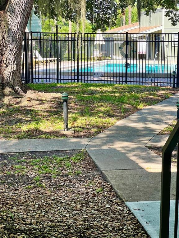 A concrete walkway leads toward a fenced swimming pool area with a large tree nearby — 310 PALM COAST PARKWAY NE UNIT 101, PALM COAST, FL