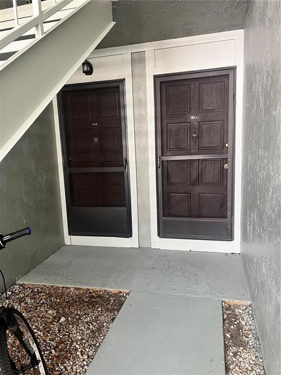 Two dark brown doors with screen doors are situated under a staircase on a patio — 310 PALM COAST PARKWAY NE UNIT 101, PALM COAST, FL