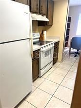 A kitchen features white appliances, dark wood cabinets, and light-colored tile flooring — 310 PALM COAST PARKWAY NE UNIT 101, PALM COAST, FL