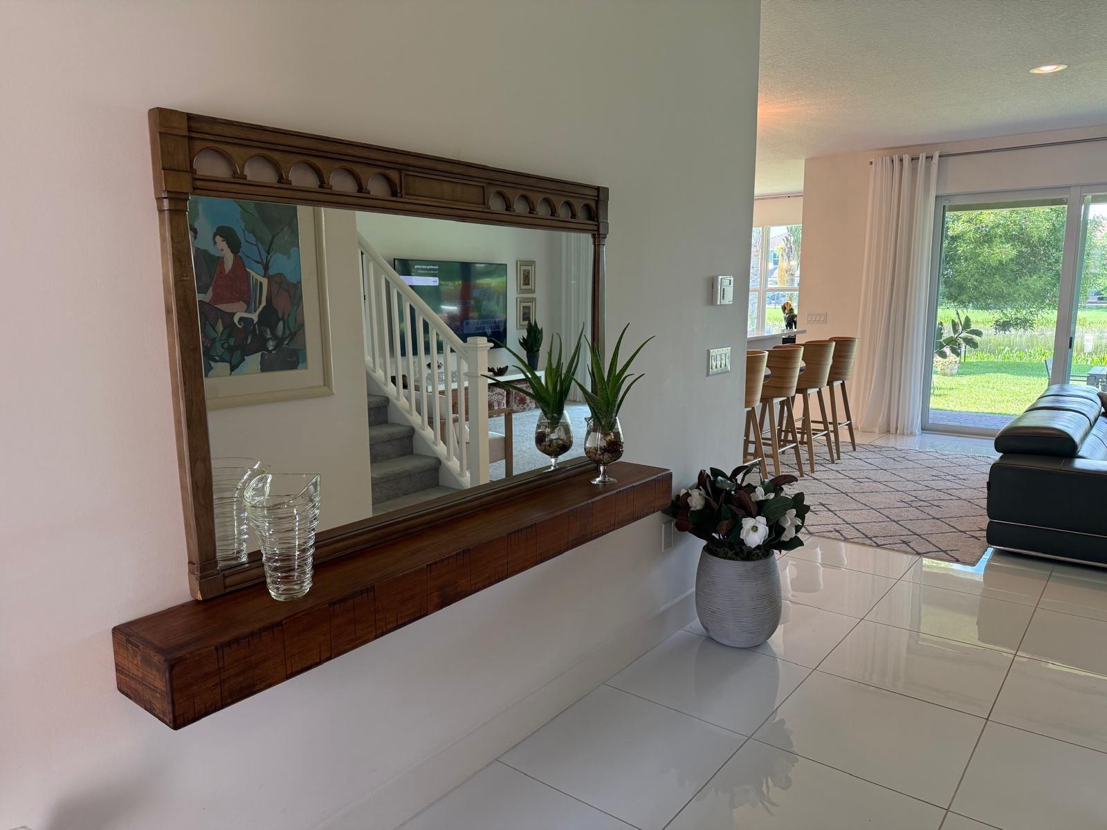 A wooden floating shelf with a large mirror hangs on a wall in a tiled entryway — 9613 Highland Pointe Pass, Delray Beach FL 33446, DELRAY BEACH, FL