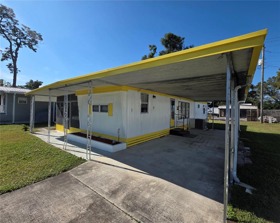 A single-story mobile home with white siding, yellow trim, and a large attached carport — 5105 CURRAN STREET, ZEPHYRHILLS, FL