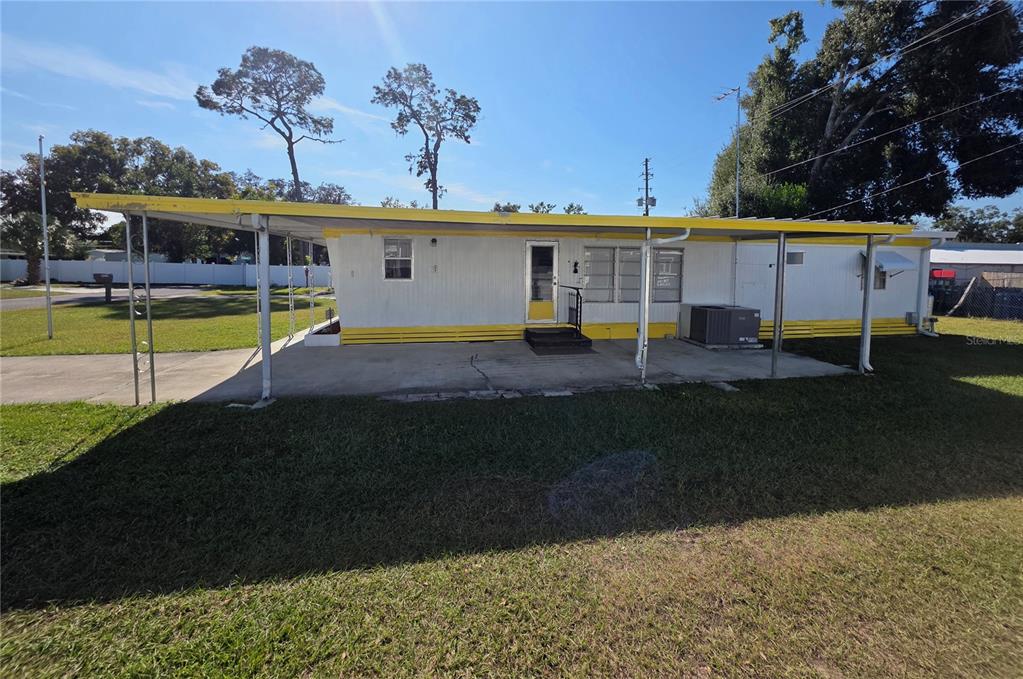 A single-story mobile home with a yellow-trimmed roof and a concrete carport — 5105 CURRAN STREET, ZEPHYRHILLS, FL