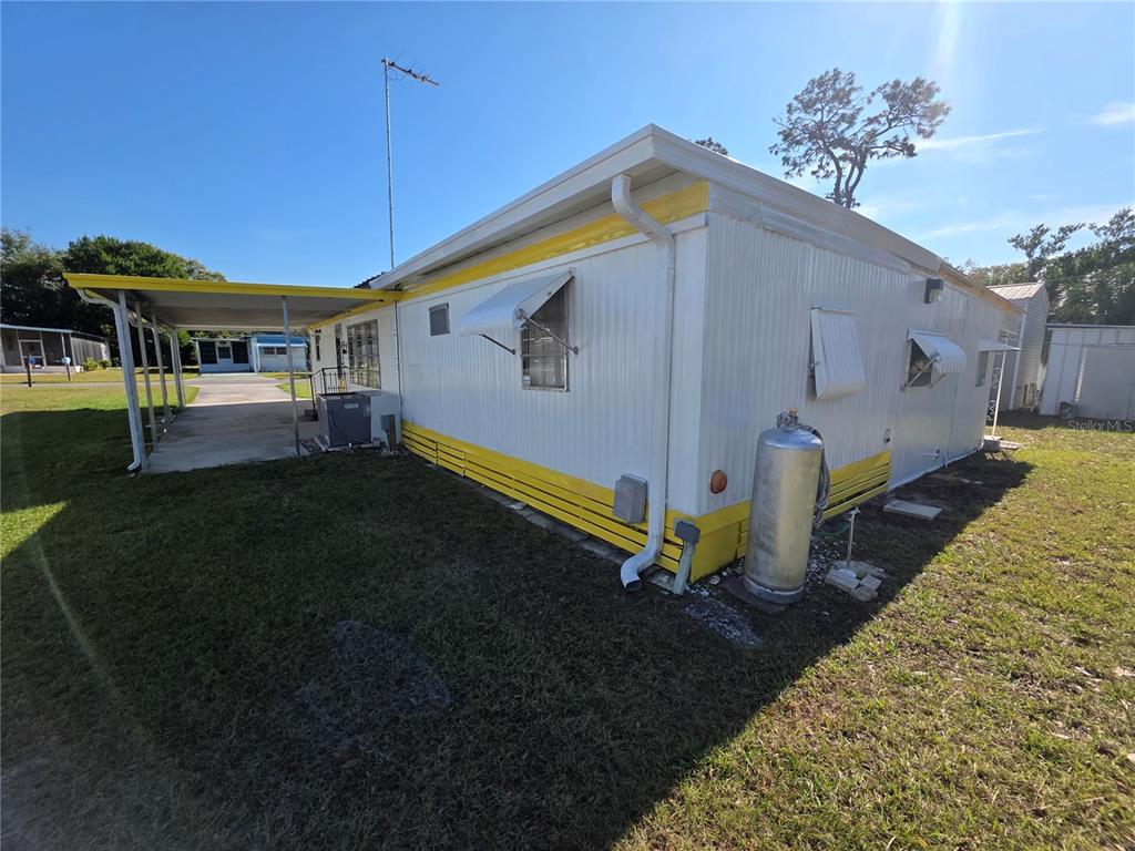 The exterior of a mobile home features white siding, yellow trim, and a metal carport — 5105 CURRAN STREET, ZEPHYRHILLS, FL