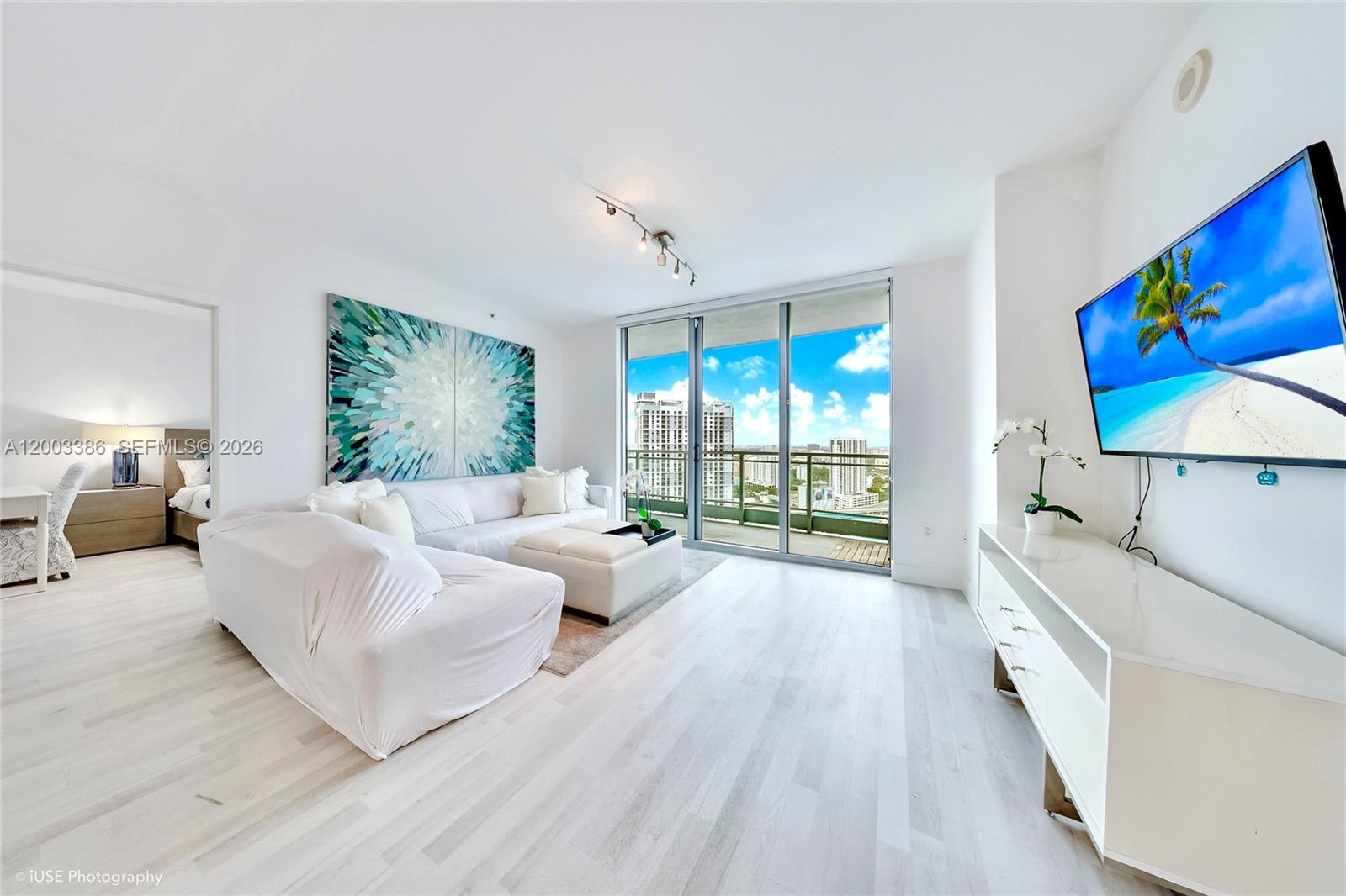 A bright living room features white furniture, light wood floors, and a balcony with city views — 90 SW 3rd St # 3109, Miami FL 33130, MIAMI, FL