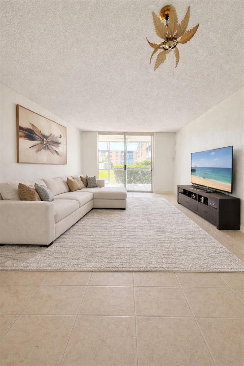A living room features a beige sectional sofa, a large area rug, and a television console — 202 SE 10th Street # 105, Dania Beach FL 33004, DANIA BEACH, FL