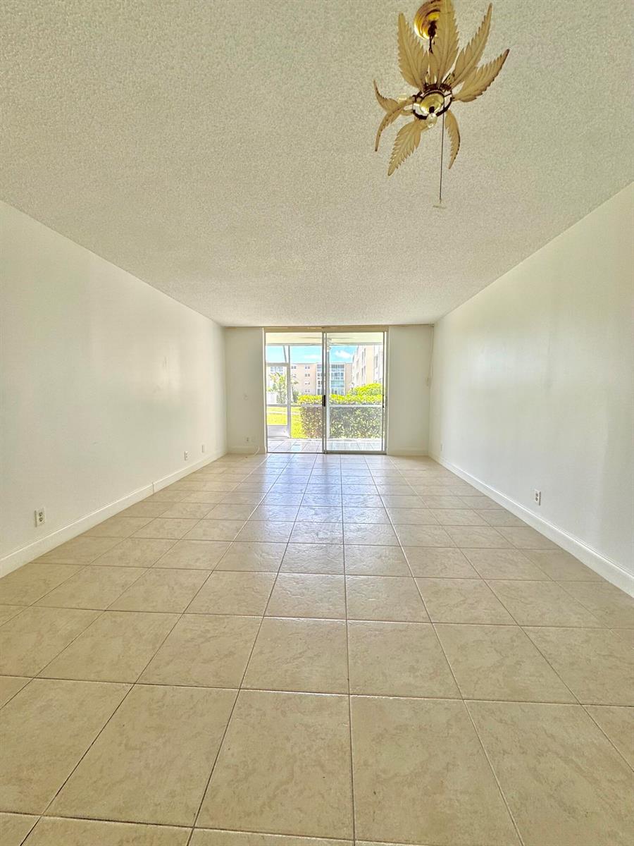 An empty living room with beige tile flooring, white walls, and a palm-leaf ceiling fan — 202 SE 10th Street # 105, Dania Beach FL 33004, DANIA BEACH, FL